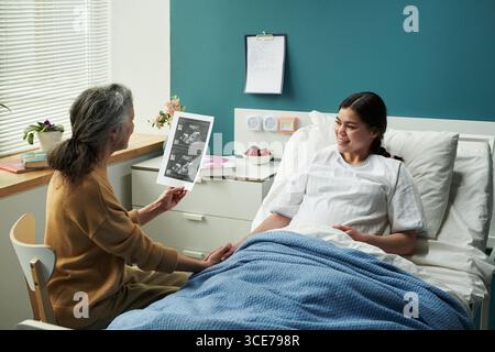Femme caucasienne senior admirant l'échographie tout en visitant sa fille enceinte Banque D'Images