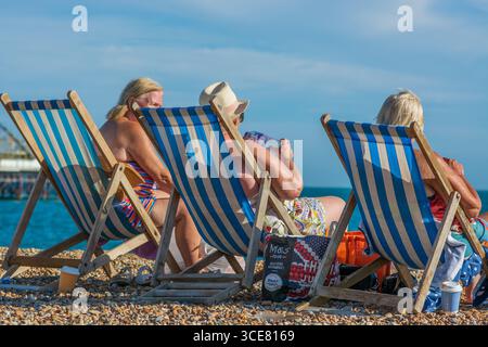 Bains de soleil dans des transats profitant d'une chaude journée d'été sur la plage de Brighton, Brighton, Angleterre, Royaume-Uni. Banque D'Images