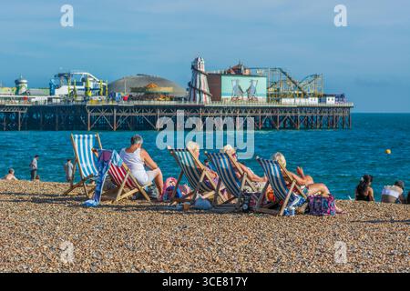 Bains de soleil dans des transats profitant d'une chaude journée d'été sur la plage de Brighton, Brighton, Angleterre, Royaume-Uni. Banque D'Images