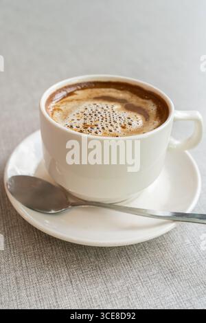 Gros plan d'une tasse à café fraîchement préparée avec dessus et cuillère mousseux Banque D'Images