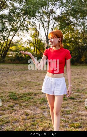 Jeune femme montrant quelque chose avec la main ouverte dans le parc pendant l'été Banque D'Images