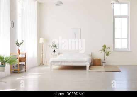 Chambre spacieuse et ensoleillée avec linge blanc et plantes vertes au design minimaliste moderne. Banque D'Images