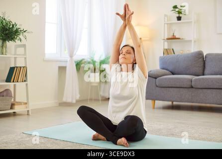 Femme senior dans la pose de lotus de yoga à la maison, l'apprentissage des poses de base, les techniques de respiration, la pratique Banque D'Images