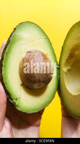 Mains tenant deux moitiés d'avocat sur fond jaune Banque D'Images