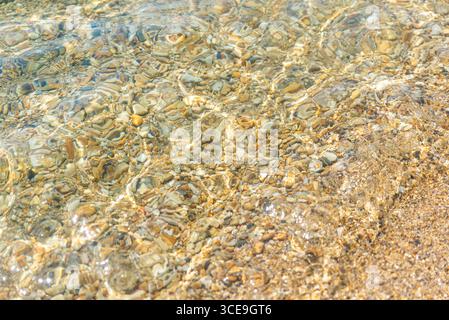Gros plan de l'eau de mer cristalline avec de petits cailloux visibles sur le fond sablonneux Banque D'Images