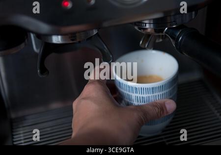 Main tenant une tasse de café fraîchement moulu de la machine à espresso Banque D'Images