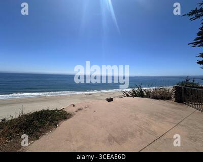 Une vue panoramique sur la côte depuis une falaise, montrant des dunes herbeuses, des maisons en bord de mer, et une longue étendue de plage de sable rencontrant les eaux bleues calmes Banque D'Images