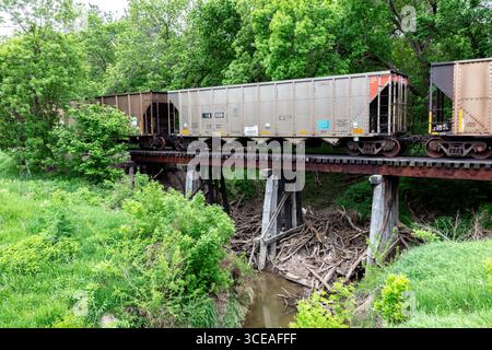 Wagons de marchandises de chemin de fer sur chevalets en bois dans le comté de Cloud, Kansas. De la vapeur coule sous le pont. Herbe verte au premier plan, arbres en arrière-plan. Banque D'Images