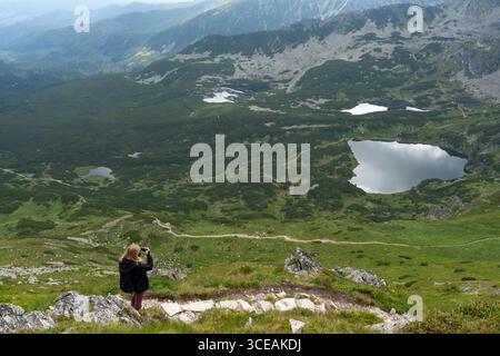 Photographe femme capturant une vue aérienne époustouflante des lacs de montagne et des vallées verdoyantes depuis le point de vue alpin. Concept de photographie de paysage Banque D'Images