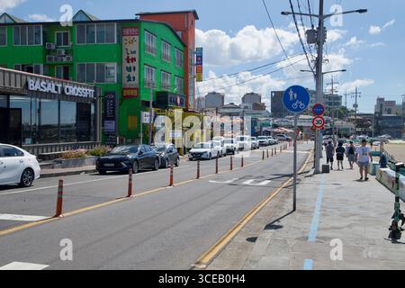 La circulation rampante le long de la route de bord de mer à Iho Tewoo Beach à côté de la promenade et de la piste cyclable, avec des hôtels colorés, des panneaux de signalisation et des piétons A. Banque D'Images