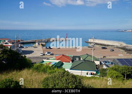 Vue surélevée sur le port de Gamundong sur la côte ouest de Jeju, montrant des quais, un phare brise-lames rouge, des voitures garées et de l'eau calme s'ouvrant vers le Ko Banque D'Images