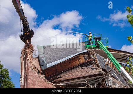 L'homme à l'aide de tuyau d'eau haute pression pour l'atténuation de la poussière comme une longue portée étendue avec l'excavateur hydraulique du bras de flèche et concasseur griffe qui démolit Alu Banque D'Images