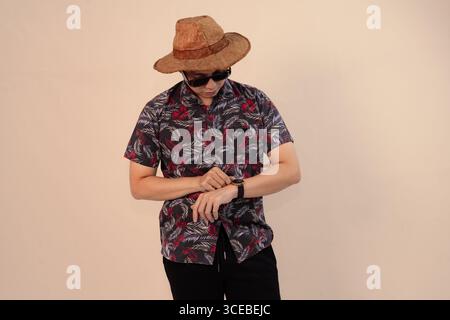 jeune homme en chemise tropicale vérifiant sa montre et portant des lunettes de soleil Banque D'Images