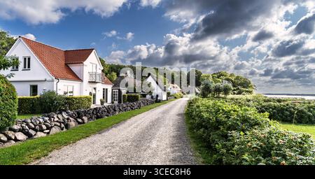 Scène rurale idyllique avec de charmants cottages le long d'une route de campagne avec une végétation luxuriante et des vues panoramiques sur les nuages ondulants. Banque D'Images