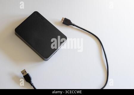 Disque dur externe noir avec son câble usb reposant sur une surface blanche Banque D'Images
