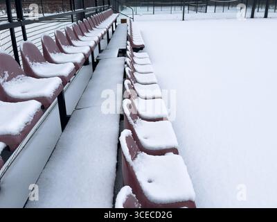 Sièges en plastique vides de stade de sport extérieur sur des supports en acier recouverts de neige en hiver Banque D'Images