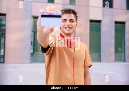 Jeune homme souriant tout en montrant une carte de visite vierge à la caméra à l'extérieur Banque D'Images