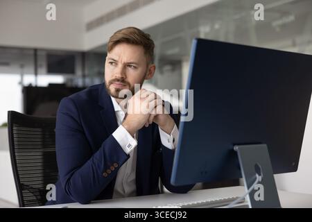 Pensif intéressé jeune homme d'affaires regardant loin, assis au bureau lieu de travail Banque D'Images