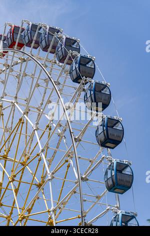 Vue captivante d'une grande roue colorée dominant un ciel bleu vif, illustrant une journée pleine de loisirs et d'aventure dans la ville vibrante Banque D'Images