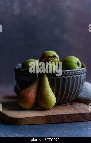 Une collection de poires sauvages fraîches exposées dans un bol décoratif en céramique, reposant sur une planche de bois. Le cadre rustique met en valeur la beauté naturelle o Banque D'Images
