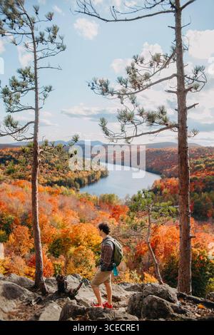 Un randonneur se tient sur un éperon rocheux, admirant le magnifique feuillage d'automne et la rivière sinueuse au Québec, Canada. Les couleurs vibrantes créent un a pittoresque Banque D'Images