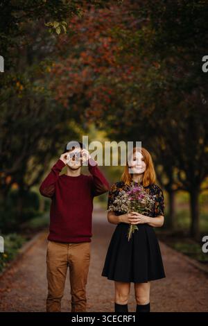 Un couple profitant d'une belle journée d'automne au Québec, Canada. La femme tient un bouquet de fleurs sauvages, tandis que l'homme regarde à travers des jumelles, entouré Banque D'Images