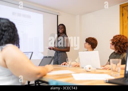 Un groupe diversifié engagé dans une présentation. Une personne se tient près d'un écran de projection, menant la discussion, tandis que les membres de l'équipe avec un ordinateur portable écoutent atte Banque D'Images