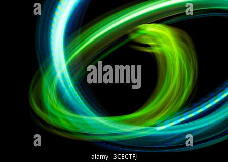 Image abstraite dynamique mettant en vedette des néons tourbillonnants dans des tons verts et bleus vifs sur un fond noir intense, créant une sensation de mouvement et Banque D'Images