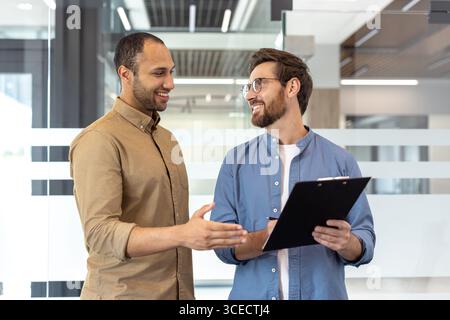 Deux professionnels debout ensemble dans un bureau discutant d'un document avec des sourires et des gestes. Banque D'Images