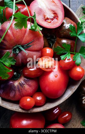 Vue de dessus des tomates mûres et du persil frais dans un bol en bois. Les tomates rouges éclatantes et le persil vert sont placés sur un fond en bois foncé, emp Banque D'Images