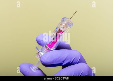 Une main gantée tient une seringue médicale sur un fond mou. L'aiguille est préparée pour l'utilisation, montrant la précision et le soin dans la pratique médicale Banque D'Images