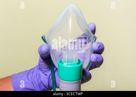 Image rapprochée d'un masque à oxygène médical tenu par une main portant des gants violets. L'arrière-plan vibrant renforce l'accent sur l'équipement sanitaire Banque D'Images