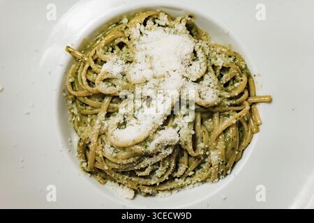 Un gros plan de pâtes crémeuses au pesto généreusement saupoudrées de parmesan râpé, servies à Venise, en Italie, capturant les riches saveurs et textures de Banque D'Images