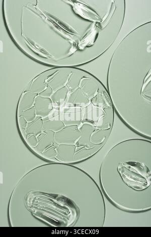 Vue de dessus des frottis de gel transparent sur verre de laboratoire disposés sur un fond vert doux, mettant en valeur les textures et la fluidité utilisées dans les soins de la peau et co Banque D'Images
