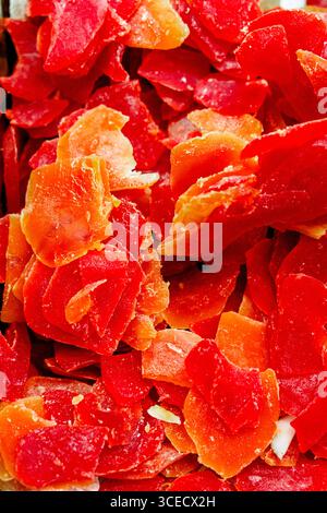 Gros plan de papayes séchées finement tranchées et éclatantes. Les teintes rouge et orange vives créent un contraste saisissant, soulignant leur douceur naturelle et Banque D'Images