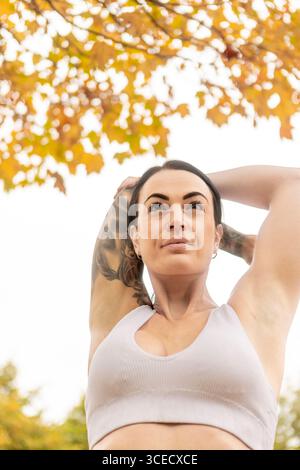 Une femme étire ses bras en faisant de l'exercice à l'extérieur pendant l'automne dans un parc néo-zélandais. Le feuillage d'automne vibrant ajoute une toile de fond pittoresque à son worko Banque D'Images
