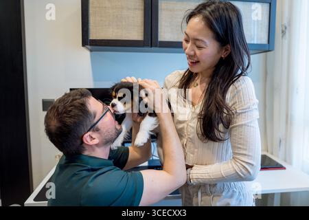Un couple diversifié profite d'un moment tendre avec leur chiot dans un cadre confortable à la maison. L'atmosphère joyeuse capture la chaleur et la joie de leur l partagé Banque D'Images