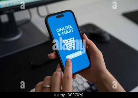 Recadrage d'une personne méconnaissable à l'aide d'un smartphone pour faire des courses en ligne à la maison. L'interface de l'application mobile affiche un panier d'achat numérique pour co Banque D'Images