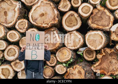 Garçon tenant une pancarte devant une pile de bûches coupées souligne le problème de la déforestation dans les bois. L'image met l'accent sur la conscience environnementale et sus Banque D'Images