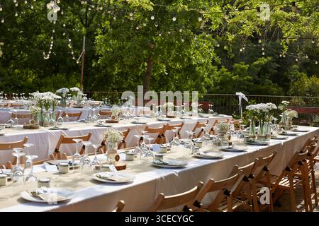 Belle configuration de table de mariage boho à l'extérieur avec des arrangements floraux blancs dans des vases en verre. Chaises et tables en bois avec vaisselle élégante créer Banque D'Images