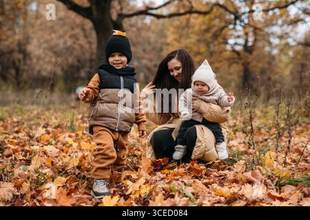Une famille joyeuse profite d'une journée d'automne dans le parc, entourée de feuilles colorées. La chaleur de la saison crée une toile de fond parfaite pour le jeu des enfants Banque D'Images