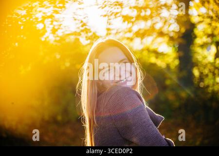 Belle femme enceinte avec des cheveux roux coulants se tient gracieusement dans un cadre naturel, entouré de lumière douce du soleil et de verdure, incarnant la sérénité et Banque D'Images