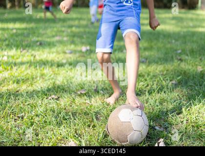 Image recadrée méconnaissable d'enfants brésiliens jouant avec enthousiasme au football sur un terrain d'herbe luxuriante pieds nus à Tres Coroas, au Brésil, capturant JO Banque D'Images
