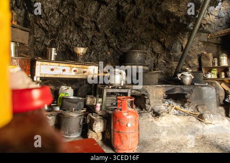 Une cuisine rustique au sein du monastère Phugtal au Ladakh, mettant en valeur des casseroles et des ustensiles de cuisine traditionnels contre un mur de pierre antique, point culminant Banque D'Images