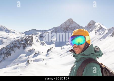 Un snowboardeur vêtu d'équipement d'hiver se tient en toute confiance dans un cadre de montagne de l'arrière-pays. La lumière du soleil améliore le paysage enneigé, idéal pour un libre Banque D'Images