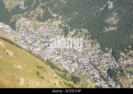 Vue aérienne du village de Zermatt entouré de collines verdoyantes et de forêts denses sous le soleil alpin de l'été. Charmants bâtiments et routes sinueuses enha Banque D'Images