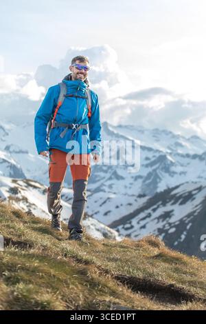Un homme marche en toute confiance à travers les Pyrénées enneigées, profitant de vues à couper le souffle et de l'air frais de la montagne. Son équipement vibrant se démarque de la sérénité Banque D'Images