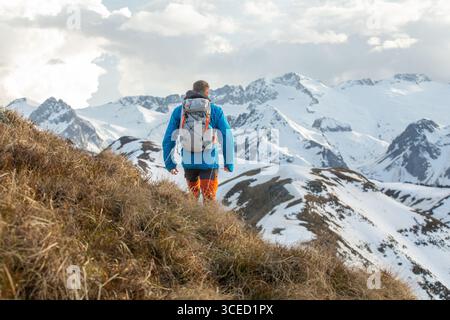 Un homme en équipement de plein air fait des randonnées le long d'un sentier pittoresque dans les montagnes des Pyrénées. Les sommets enneigés créent une toile de fond à couper le souffle, capturant l'esprit de Banque D'Images
