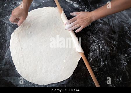 Une vue rapprochée des mains qui déroulent la pâte sur une table en bois. Banque D'Images
