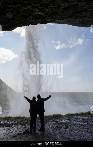 Islande, Sud de l'Islande. Seljalandsfoss, la cascade la plus connue du sud-ouest de l'Islande. Couple sous cascade. Banque D'Images